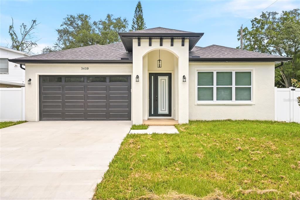 A single-story house features a white stucco exterior, a dark garage door, and a covered entryway — 3410 N 31ST STREET, TAMPA, FL