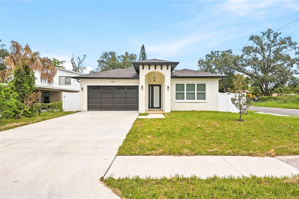 A single-story house with a white stucco exterior, dark garage door, and a covered entryway — 3410 N 31ST STREET, TAMPA, FL