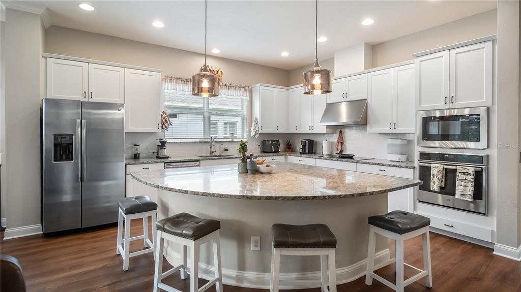 A kitchen features white cabinetry, stainless steel appliances, and a large curved granite island — 16451 GOOD HEARTH BOULEVARD, CLERMONT, FL