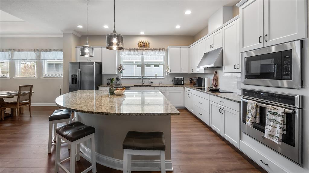 A modern kitchen features white cabinetry, granite countertops, stainless steel appliances, and a large island — 16451 GOOD HEARTH BOULEVARD, CLERMONT, FL