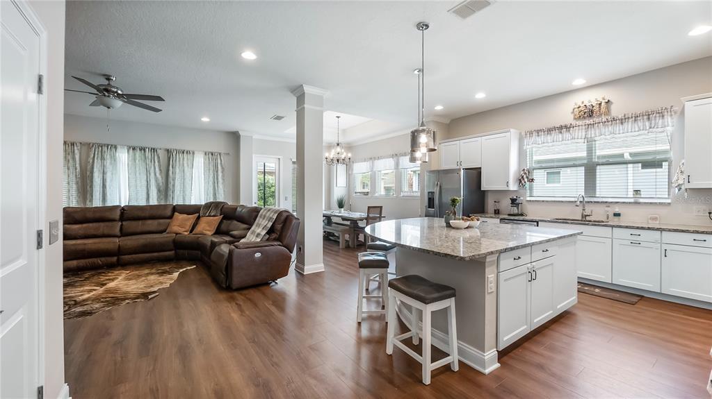 A spacious open-concept kitchen and living area features white cabinetry, granite countertops, and wood flooring — 16451 GOOD HEARTH BOULEVARD, CLERMONT, FL