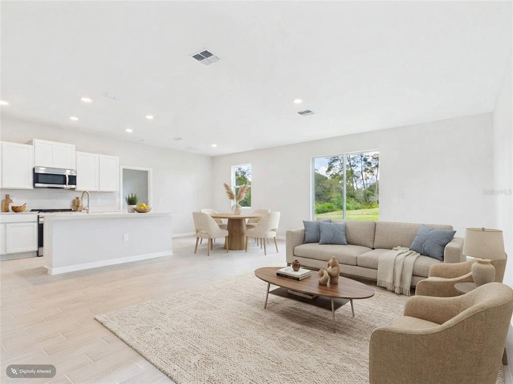 An open-concept kitchen and living area with white cabinets, light tile flooring, and sliding doors — 16090 SW 42ND TERRACE, OCALA, FL