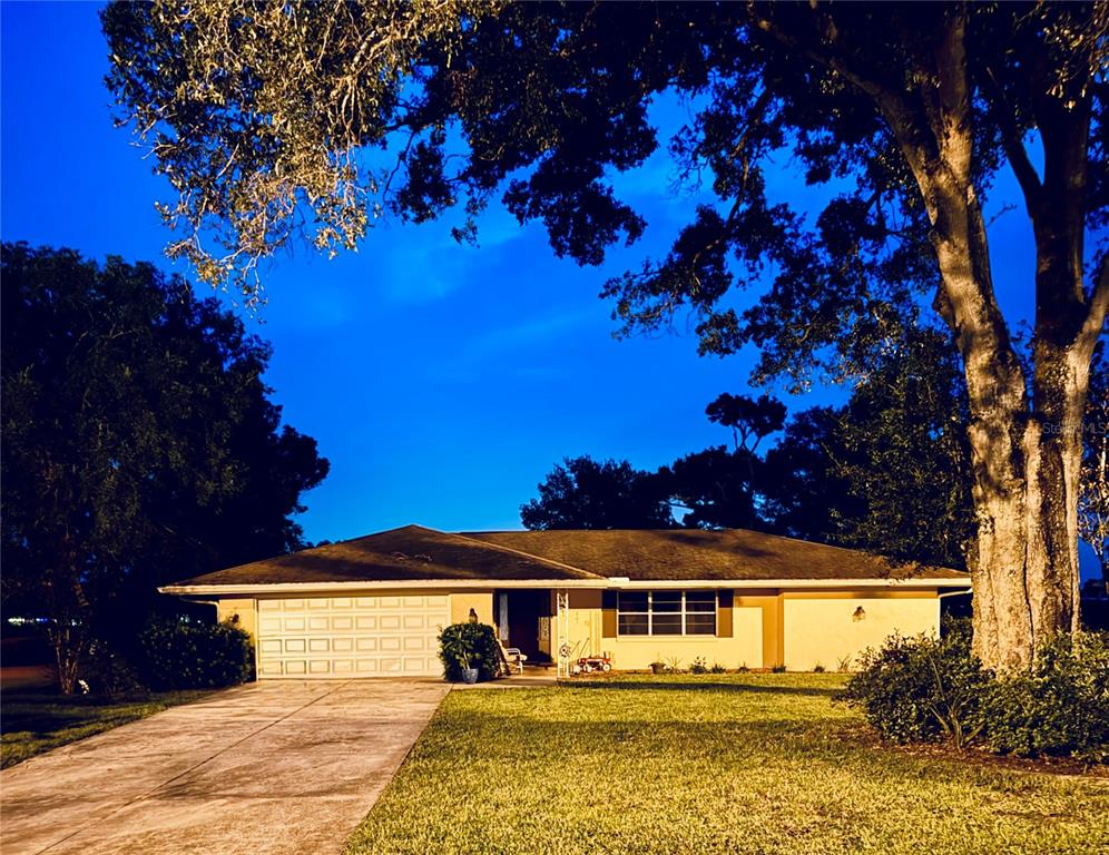 A single-story house with a garage and a large tree at dusk — 6088 FAIRWAY DRIVE, RIDGE MANOR, FL