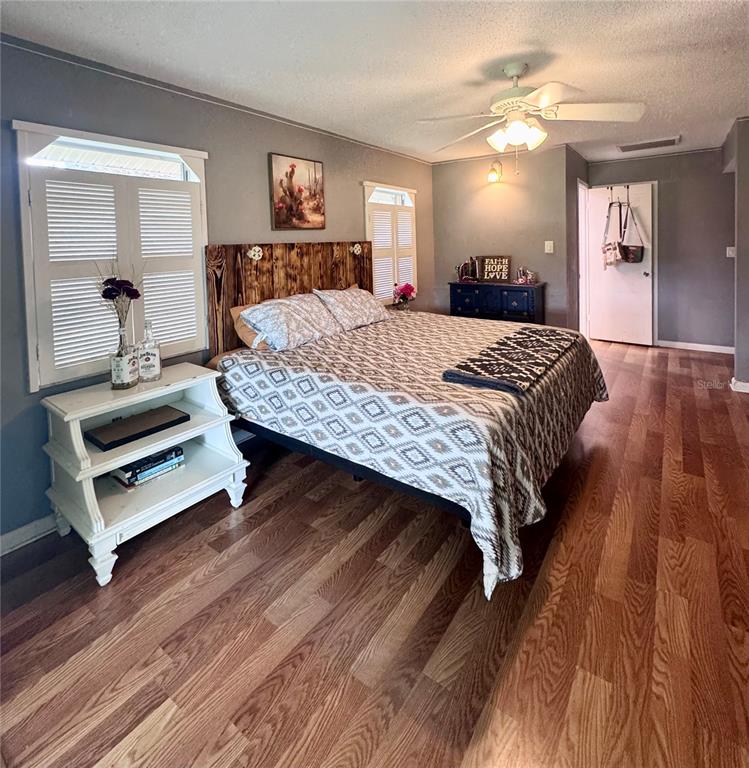 A bedroom features a wooden headboard, a patterned bedspread, white nightstand, and wood-look flooring — 6088 FAIRWAY DRIVE, RIDGE MANOR, FL