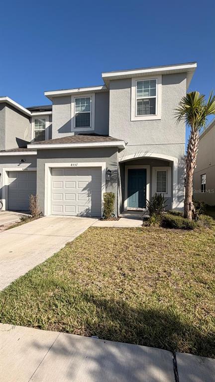 A two-story gray stucco townhouse features a single-car garage and a small front lawn — 4557 TEOLI COURT, KISSIMMEE, FL