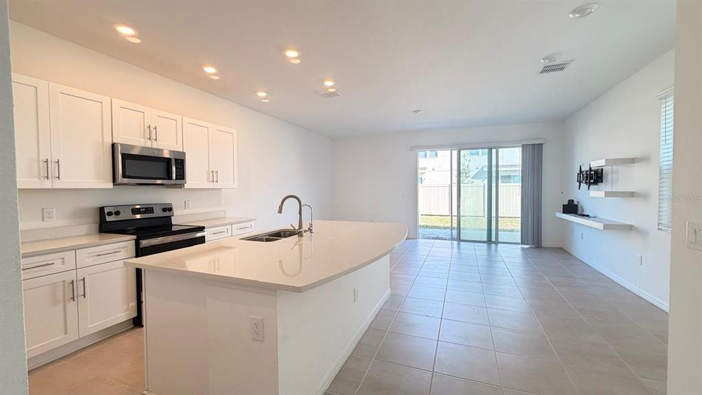 A kitchen with white cabinets and a large island opens into a tiled living area — 4557 TEOLI COURT, KISSIMMEE, FL