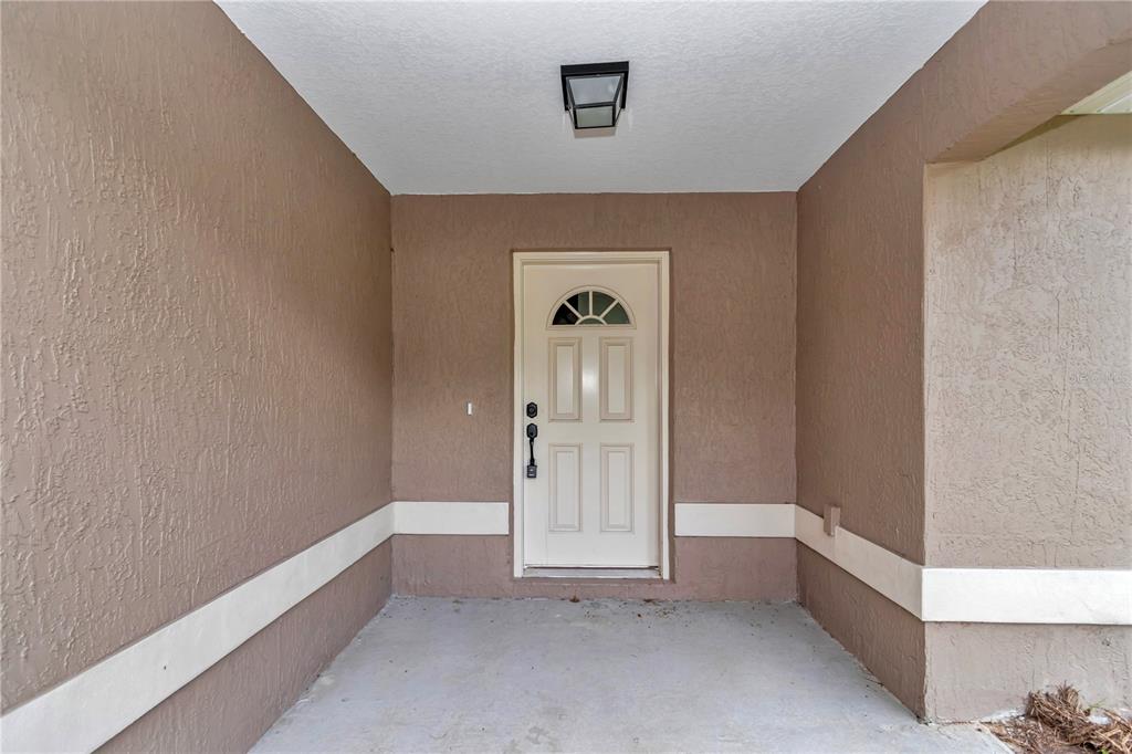 A covered concrete entryway features tan stucco walls, a white door, and a ceiling light — 64 MALAUKA ROAD, OCKLAWAHA, FL