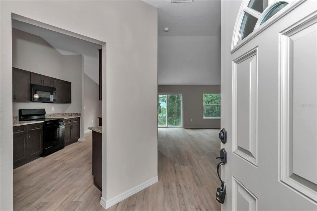 An entryway opens into a kitchen with dark cabinets and a living area with light flooring — 64 MALAUKA ROAD, OCKLAWAHA, FL