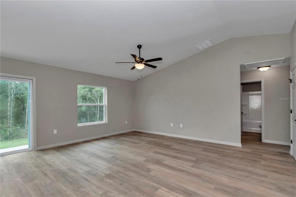 A spacious room features light gray walls, wood-look flooring, a ceiling fan, and sliding doors — 64 MALAUKA ROAD, OCKLAWAHA, FL