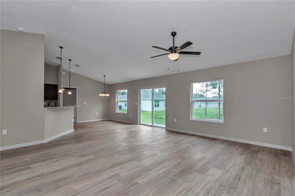 An open-concept living area features light wood-look flooring, neutral walls, a ceiling fan, and sliding doors — 64 MALAUKA ROAD, OCKLAWAHA, FL
