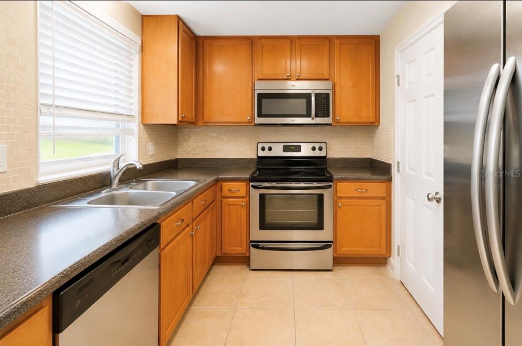 A kitchen features wood cabinets, stainless steel appliances, a black refrigerator, and tile flooring — 4312 HECTOR COURT UNIT 4, ORLANDO, FL