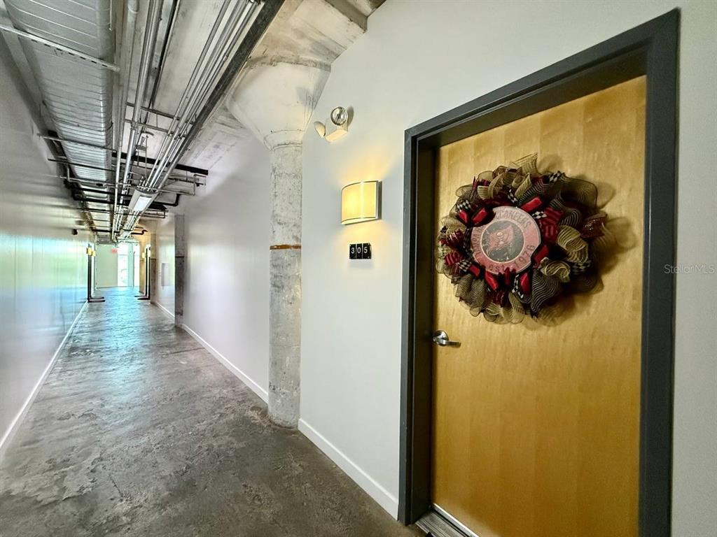 A hallway with exposed ceiling pipes, concrete flooring, and a door marked 305 — 101 N 12TH STREET UNIT 305, TAMPA, FL
