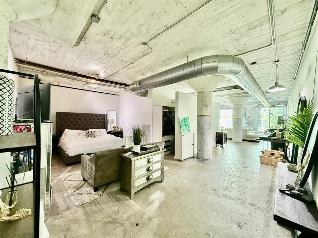 An open-concept loft bedroom with concrete ceilings, exposed ductwork, and a tufted headboard — 101 N 12TH STREET UNIT 305, TAMPA, FL