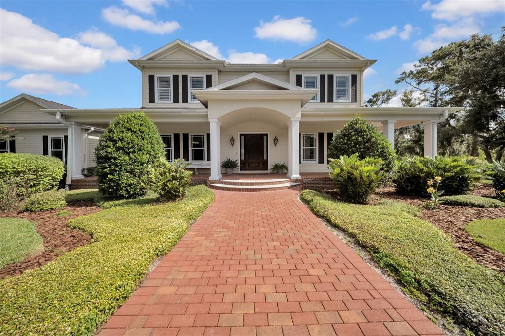 A brick walkway leads to the front entrance of a two-story house with white siding — 17930 DORMAN ROAD, LITHIA, FL