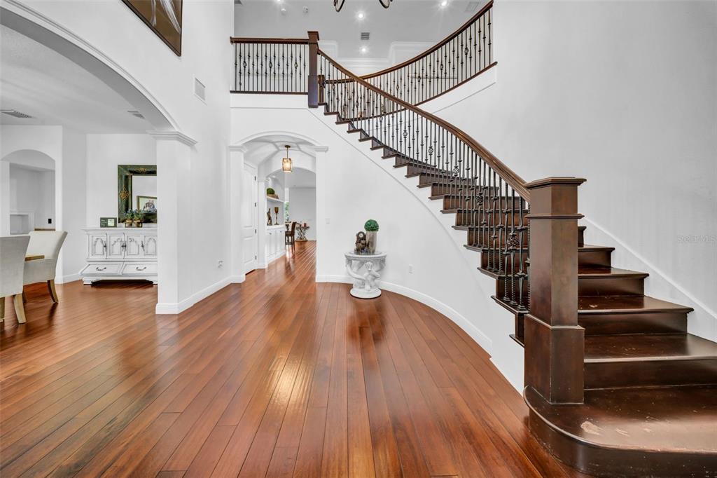 A grand foyer features hardwood floors, a curved staircase with iron railings, and white walls — 17930 DORMAN ROAD, LITHIA, FL
