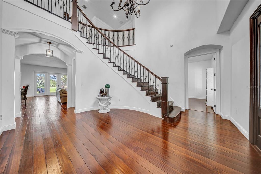A grand foyer features a curved wooden staircase, dark hardwood floors, and a crystal chandelier — 17930 DORMAN ROAD, LITHIA, FL