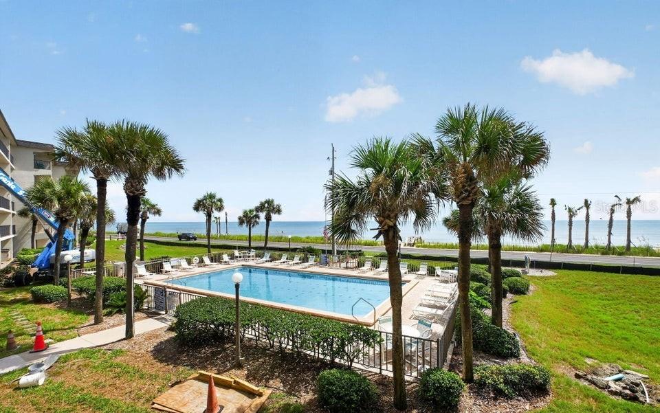 An outdoor swimming pool is surrounded by palm trees with an ocean view beyond — 2700 OCEAN SHORE BOULEVARD UNIT 208, ORMOND BEACH, FL