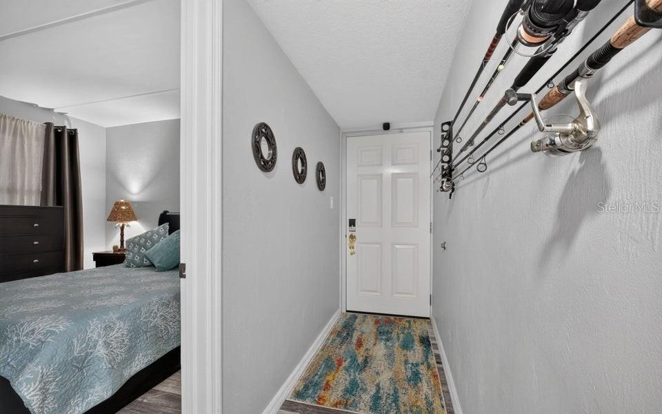 A hallway with fishing rod racks on the wall leads to a bedroom and front door — 2700 OCEAN SHORE BOULEVARD UNIT 208, ORMOND BEACH, FL