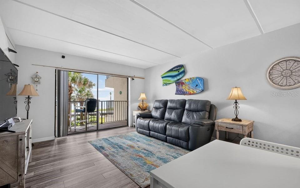 A living room features a dark leather sofa, a patterned rug, and a sliding glass door — 2700 OCEAN SHORE BOULEVARD UNIT 208, ORMOND BEACH, FL