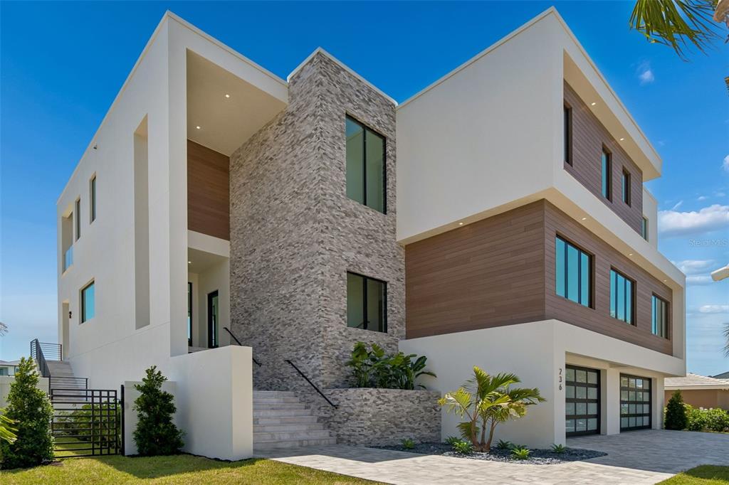 A modern multi-story house features white stucco, wood paneling, and a stone-clad facade — 236 HOWARD DRIVE, BELLEAIR BEACH, FL