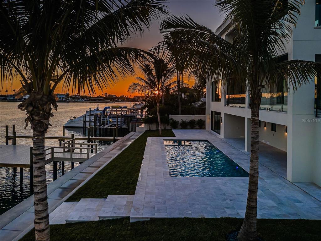 A modern waterfront home features a rectangular swimming pool, stone patio, and private boat dock — 236 HOWARD DRIVE, BELLEAIR BEACH, FL
