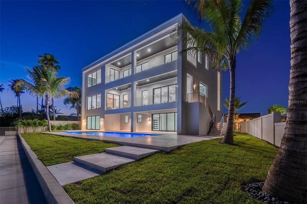 A modern three-story house with balconies and a swimming pool at dusk — 236 HOWARD DRIVE, BELLEAIR BEACH, FL
