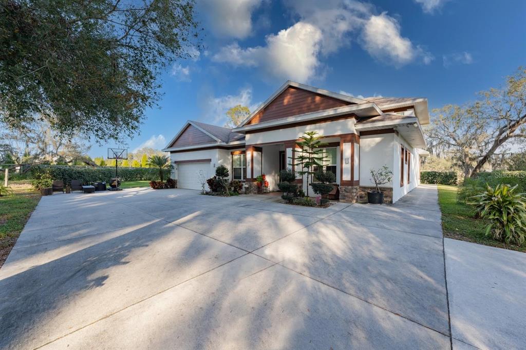 A single-story house with a large concrete driveway, white stucco walls, and brown wood accents — 9606 RIPLEY ROAD, THONOTOSASSA, FL
