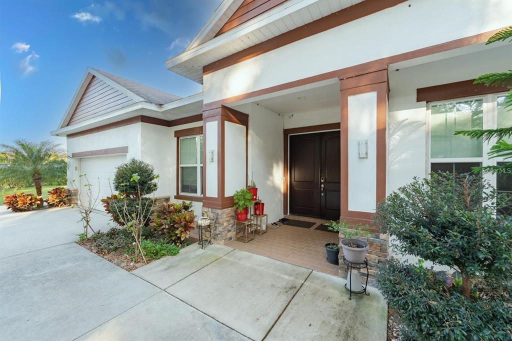 A house exterior features a covered entryway with double doors, stone accents, and a concrete driveway — 9606 RIPLEY ROAD, THONOTOSASSA, FL