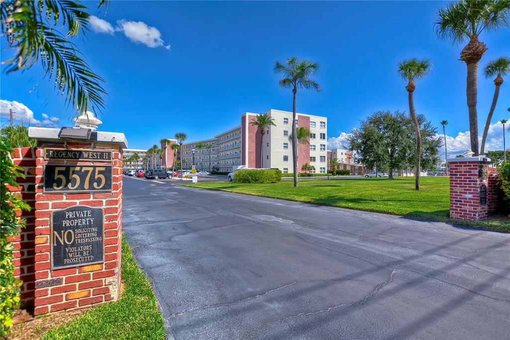 The entrance to a residential complex features a brick sign and palm trees — 5575 GULF BOULEVARD UNIT 323, ST PETE BEACH, FL
