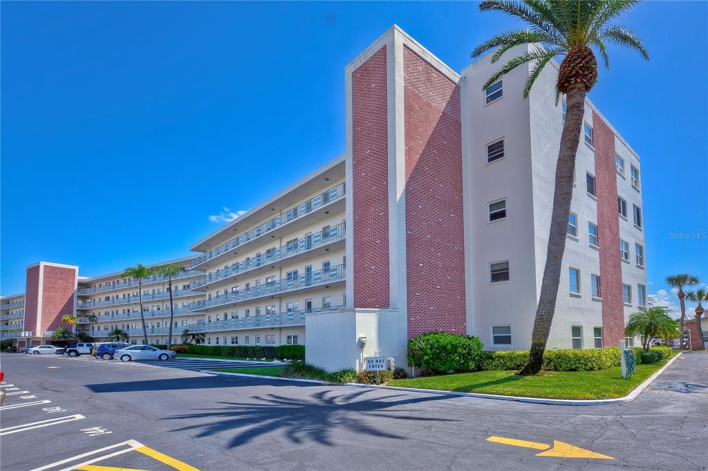 A multi-story apartment building with brick accents, balconies, and a palm tree in the foreground — 5575 GULF BOULEVARD UNIT 323, ST PETE BEACH, FL