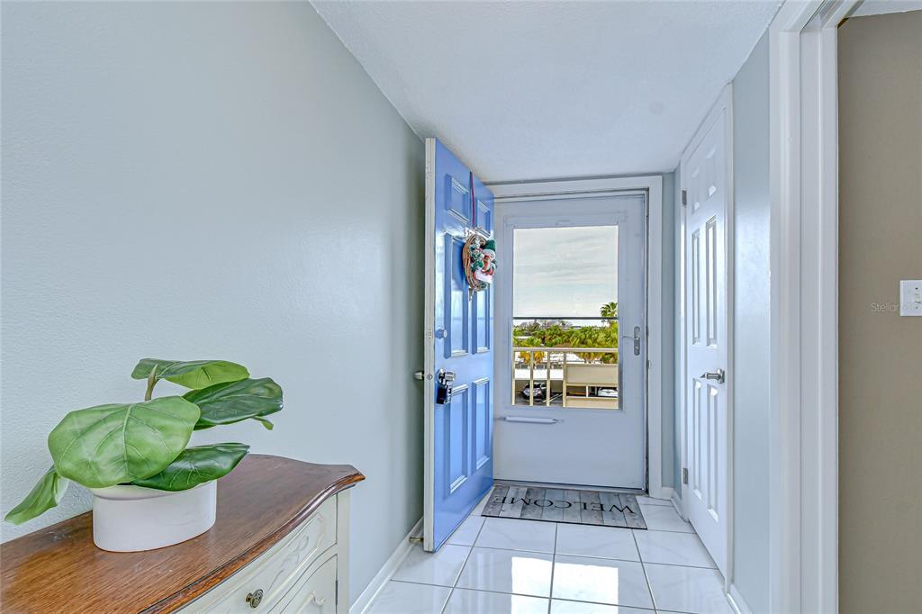 An entryway features a blue door, white tile flooring, a potted plant, and a balcony view — 5575 GULF BOULEVARD UNIT 323, ST PETE BEACH, FL