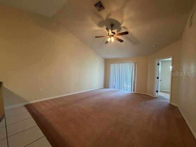 An empty living room features beige carpeting, a vaulted ceiling with a fan, and sliding doors — 33 E ST LOUIS AVENUE, EUSTIS, FL