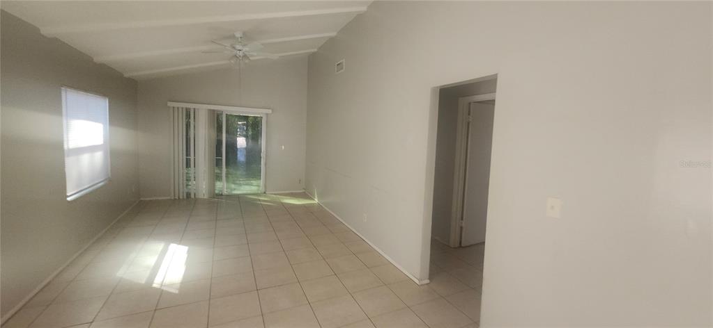 An empty living room features light tile flooring, vaulted ceilings, and a sliding glass door — 4839 BILLY DIRECT LANE, LUTZ, FL