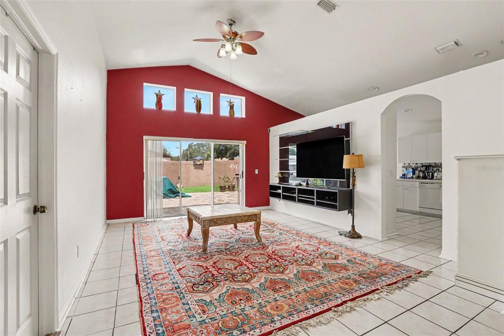 A living room features a red accent wall, tiled floors, a large rug, and sliding doors — 1102 VINETREE DRIVE, BRANDON, FL
