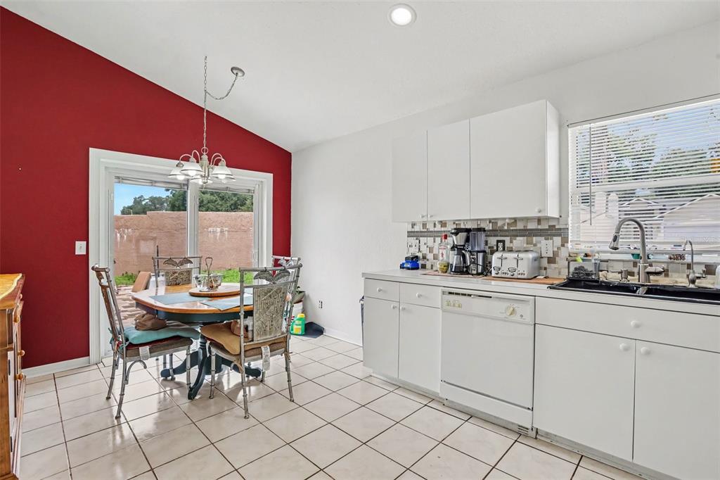 A kitchen and dining area with white cabinets, tile flooring, and a red accent wall — 1102 VINETREE DRIVE, BRANDON, FL