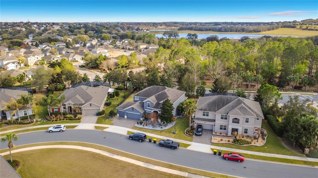 An aerial view shows three suburban houses with driveways and cars along a curved street — 539 TIMBERVALE TRAIL, CLERMONT, FL