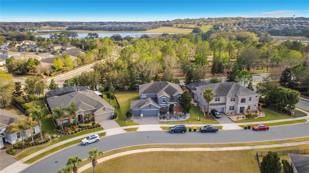 An aerial view shows three suburban houses with driveways and lawns near a wooded area — 539 TIMBERVALE TRAIL, CLERMONT, FL