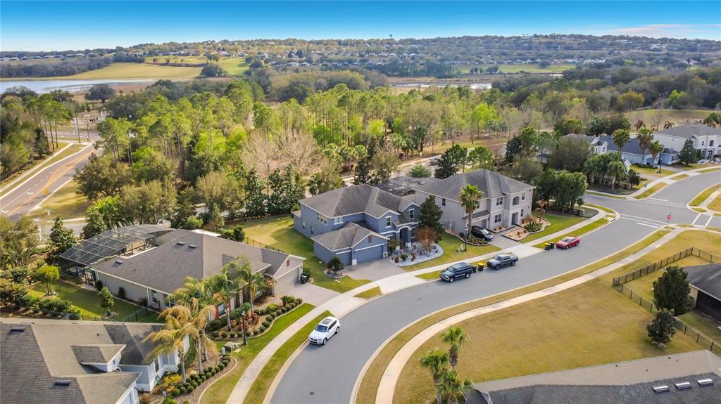An aerial view shows suburban houses with driveways and swimming pools near a wooded area — 539 TIMBERVALE TRAIL, CLERMONT, FL