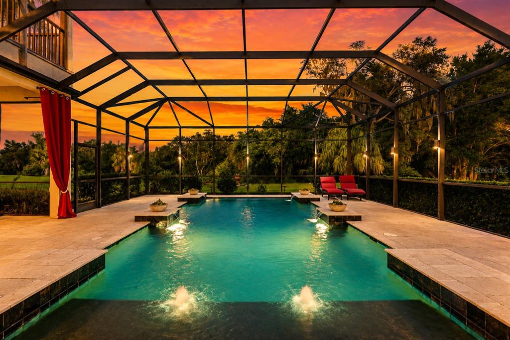 A screened-in swimming pool with fountains and lounge chairs under a vibrant sunset sky — 1568 HICKORY VIEW CIRCLE, PARRISH, FL
