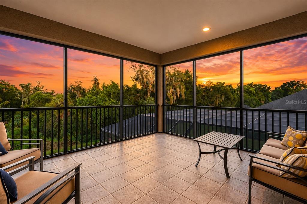 A screened-in balcony with tile flooring overlooks a sunset view of trees and rooftops — 1568 HICKORY VIEW CIRCLE, PARRISH, FL