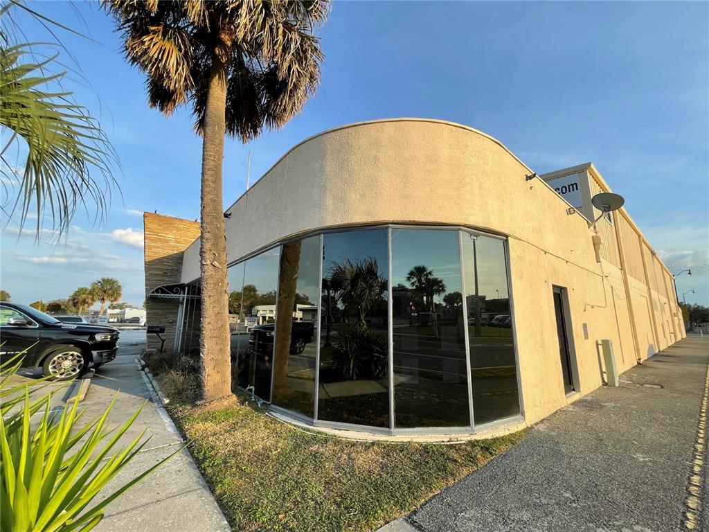 A curved glass storefront on a beige commercial building with a palm tree in front — 201 E MAIN STREET UNIT 101, LEESBURG, FL