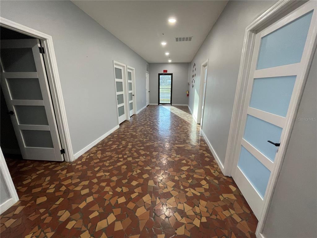 A hallway with light gray walls, white doors, and a brown mosaic tile floor — 201 E MAIN STREET UNIT 101, LEESBURG, FL