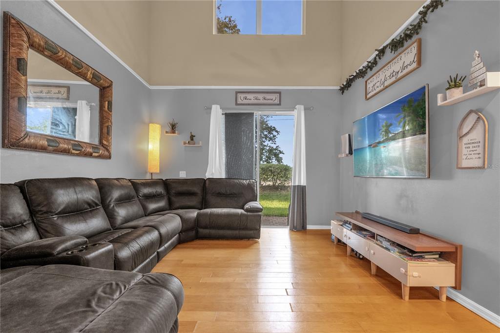 A living room features a large sectional sofa, hardwood floors, a television, and vaulted ceilings — 4981 ALITA TERRACE, ST CLOUD, FL