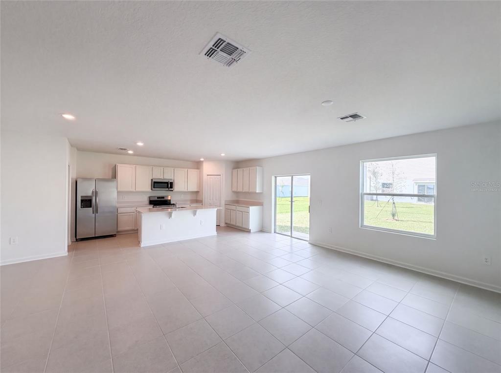 A kitchen with white cabinets and stainless steel appliances opens into a tiled living area — 2142 LASSO LOOP, EAGLE LAKE, FL