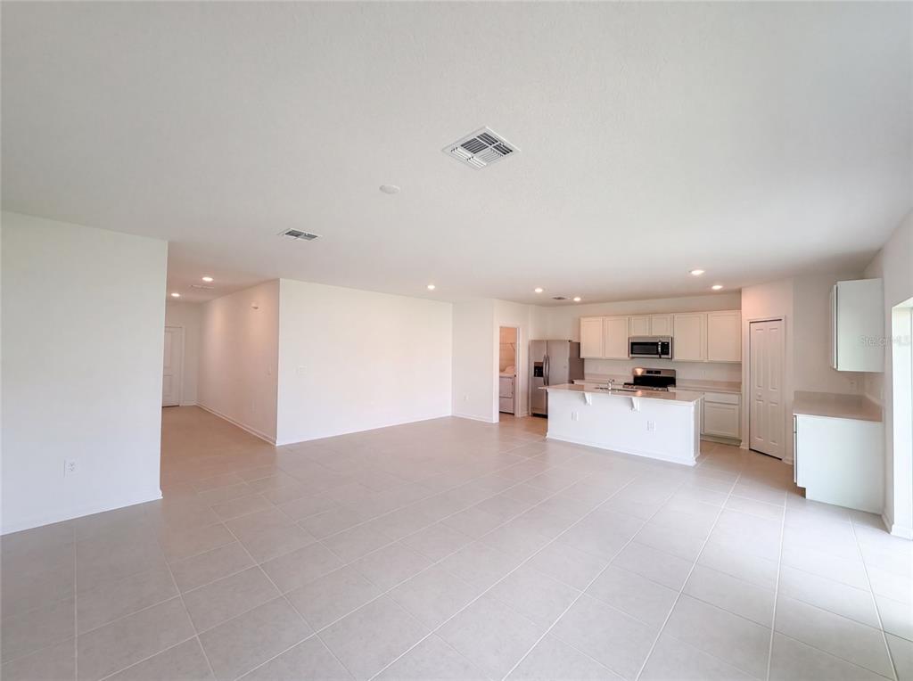 An open-concept kitchen and living area features white cabinetry, light countertops, and neutral tile flooring — 2142 LASSO LOOP, EAGLE LAKE, FL