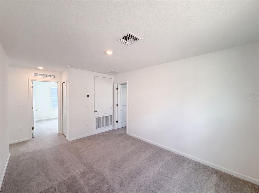 An empty room with gray carpet, white walls, a ceiling vent, and two open doorways — 2142 LASSO LOOP, EAGLE LAKE, FL