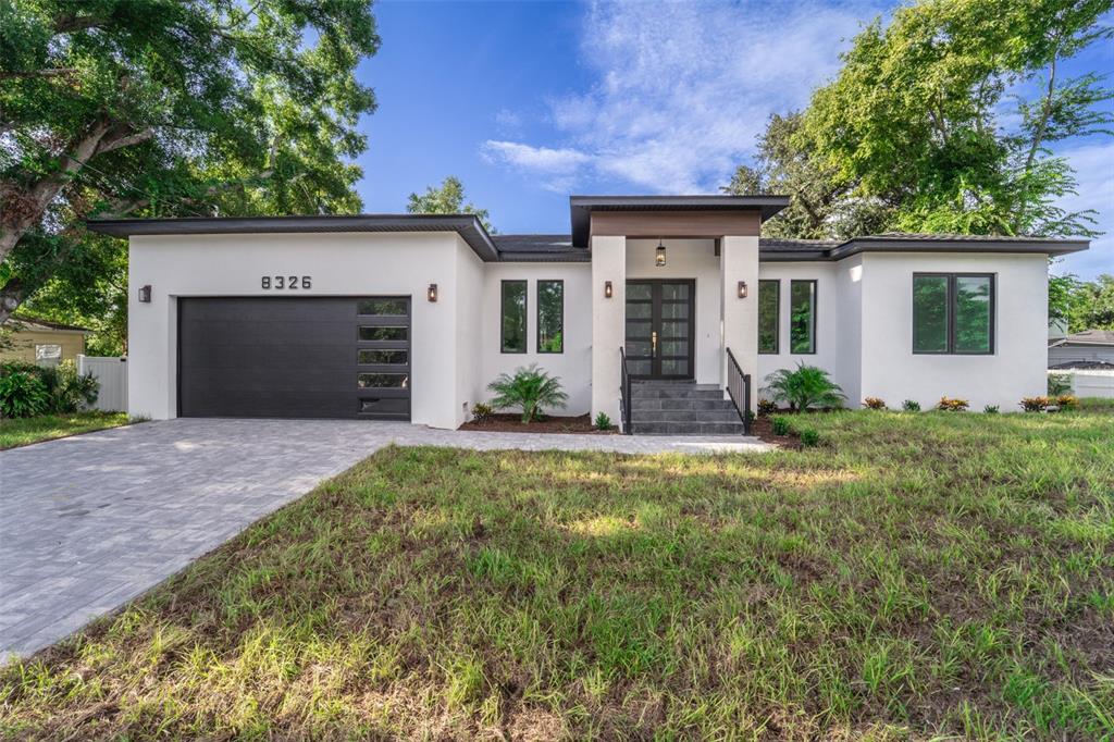 A modern single-story house with a white stucco exterior, dark garage door, and paved driveway — 8326 JUNE STREET, TAMPA, FL