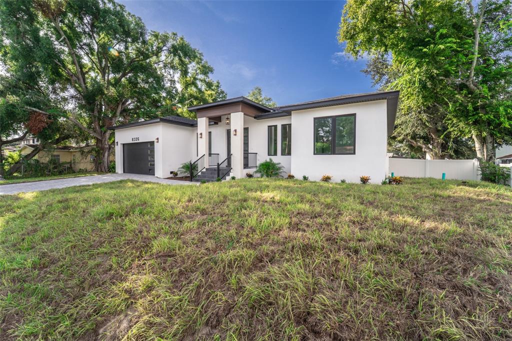 A modern, single-story white house with a dark garage door and a covered front entryway — 8326 JUNE STREET, TAMPA, FL