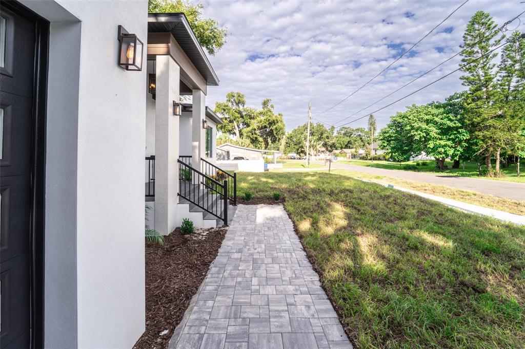 A paved walkway leads to the front entrance of a modern white house with stairs — 8326 JUNE STREET, TAMPA, FL