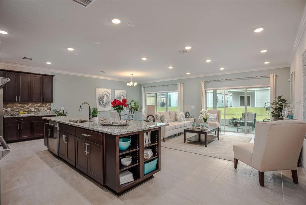 A kitchen with a large island and dark cabinets opens into a bright living area — 8600 OAKSTONE CIRCLE, LEESBURG, FL